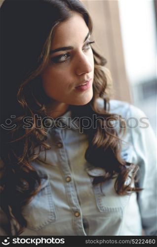 Portrait of beautiful young woman looking through the window wearing denim shirt