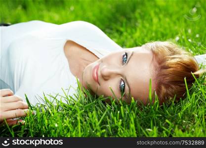 Portrait of beautiful young woman lying on a fresh green lawn