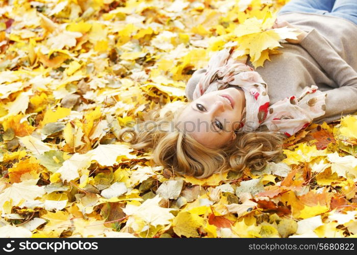 Portrait of beautiful young woman lying outdoors in autumn park