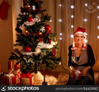 Portrait of beautiful young woman near Christmas tree holding gift&#xA;