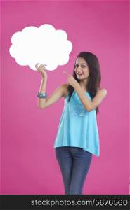 Portrait of beautiful young woman pointing at thought bubble over pink background