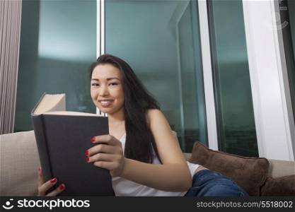 Portrait of beautiful young woman reading book in living room