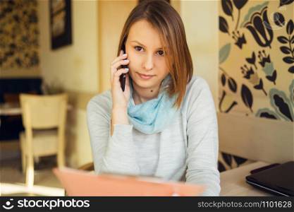 Portrait of beautiful young woman sitting by the table at cafe talking making a call using smart mobile phone
