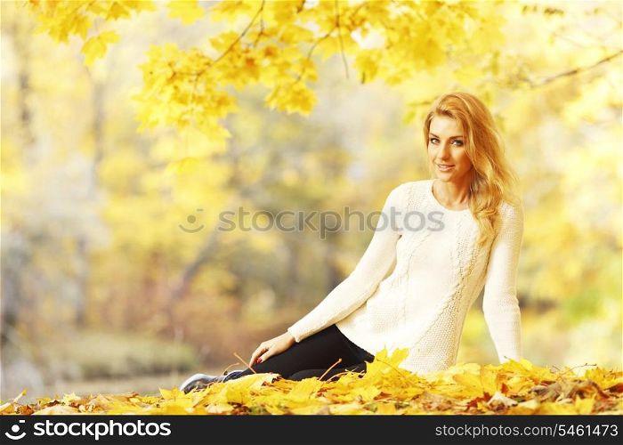 Portrait of beautiful young woman sitting outdoors in autumn park