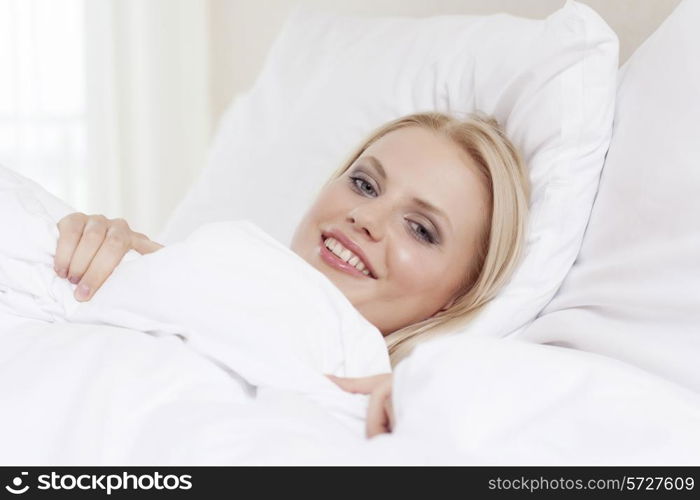 Portrait of beautiful young woman smiling while lying in bed