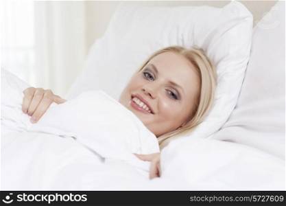 Portrait of beautiful young woman smiling while lying in bed