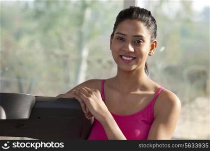 Portrait of beautiful young woman smiling while standing by a treadmill