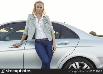 Portrait of beautiful young woman standing by car at countryside