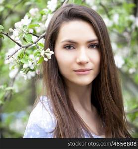 Portrait of Beautiful young woman standing near blooming trees in spring garden