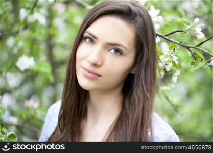Portrait of Beautiful young woman standing near blooming trees in spring garden