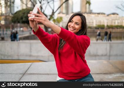 Portrait of beautiful young woman taking selfies with her mophile phone outdoors.