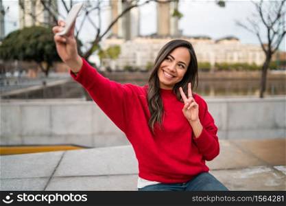 Portrait of beautiful young woman taking selfies with her mophile phone outdoors.