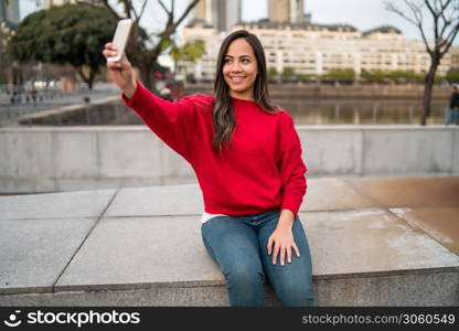 Portrait of beautiful young woman taking selfies with her mophile phone outdoors.