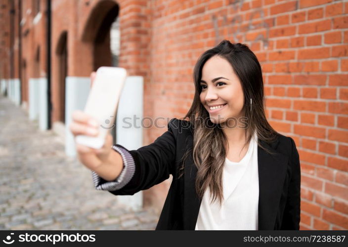 Portrait of beautiful young woman taking selfies with her mophile phone outdoors. Urban concept.