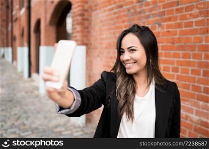 Portrait of beautiful young woman taking selfies with her mophile phone outdoors. Urban concept.