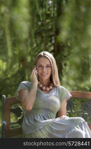 Portrait of beautiful young woman using mobile phone on park bench