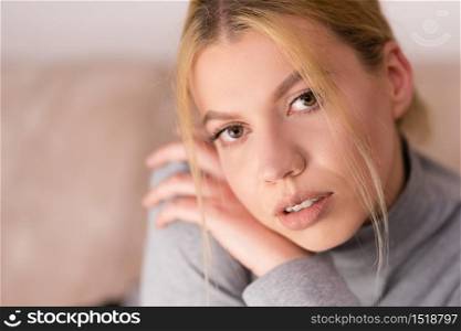 Portrait of beautiful young woman with blonde hair looking to the camera at home