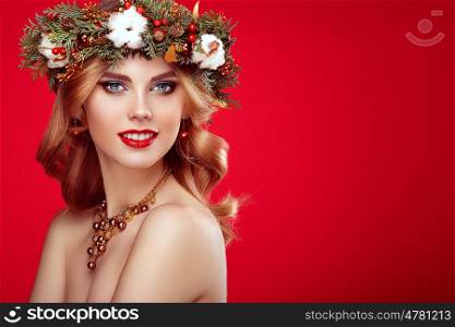 Portrait of beautiful young woman with Christmas wreath. Beautiful New Year and Christmas tree holiday hairstyle and makeup. Beauty girl portrait isolated on red background. Colorful makeup and hair