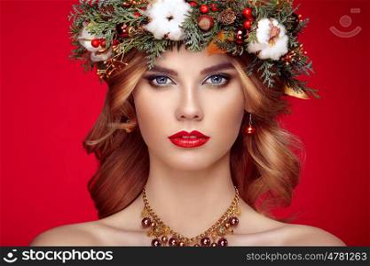 Portrait of beautiful young woman with Christmas wreath. Beautiful New Year and Christmas tree holiday hairstyle and makeup. Beauty girl portrait isolated on red background. Colorful makeup and hair