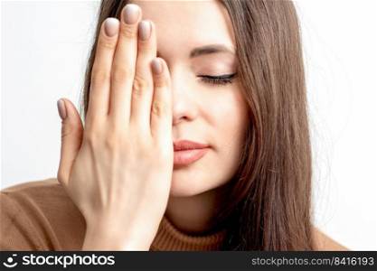 Portrait of beautiful young woman with closed eyes covering one eye by her hand on white background. Woman with closed eyes covering one eye