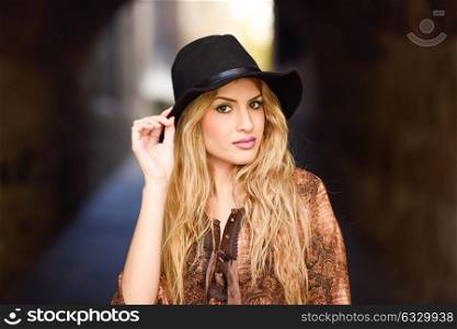 Portrait of beautiful young woman with curly hair. Girl wearing shirt and hat in urban background.