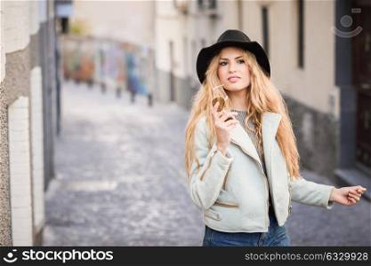 Portrait of beautiful young woman with curly hair and. Girl wearing jacket and hat in urban background.