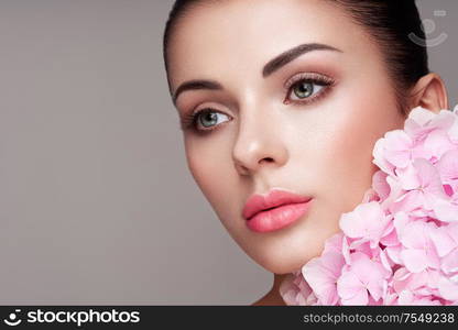 Portrait of beautiful young woman with flowers. Brunette woman with luxury makeup. Perfect skin. Eyelashes. Cosmetic eyeshadow