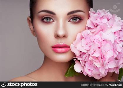 Portrait of beautiful young woman with flowers. Brunette woman with luxury makeup. Perfect skin. Eyelashes. Cosmetic eyeshadow
