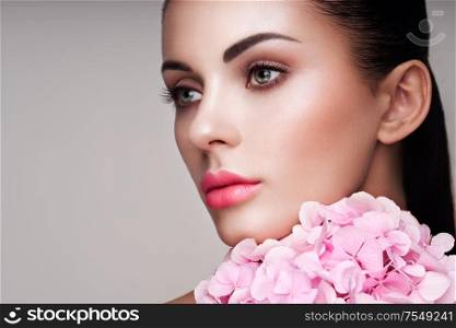 Portrait of beautiful young woman with flowers. Brunette woman with luxury makeup. Perfect skin. Eyelashes. Cosmetic eyeshadow
