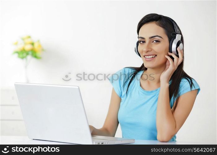 Portrait of beautiful young woman with laptop listening to headphones at home