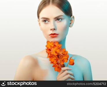 Portrait of beautiful young woman with orchid. Brunette woman with luxury makeup. Perfect skin. Eyelashes. Cosmetic eyeshadow. Orange flowers