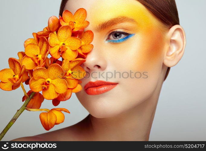 Portrait of beautiful young woman with orchid. Brunette woman with luxury makeup. Perfect skin. Eyelashes. Cosmetic eyeshadow. Orange flowers