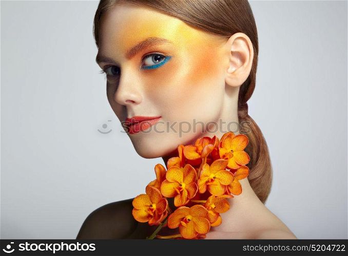 Portrait of beautiful young woman with orchid. Brunette woman with luxury makeup. Perfect skin. Eyelashes. Cosmetic eyeshadow. Orange flowers