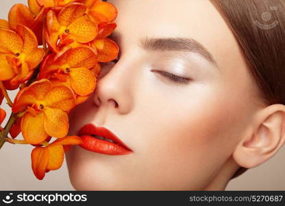 Portrait of beautiful young woman with orchid. Brunette woman with luxury makeup. Perfect skin. Eyelashes. Cosmetic eyeshadow. Orange flowers