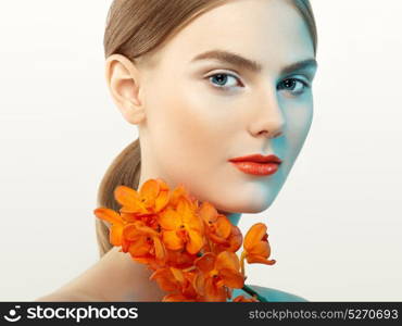 Portrait of beautiful young woman with orchid. Brunette woman with luxury makeup. Perfect skin. Eyelashes. Cosmetic eyeshadow. Orange flowers