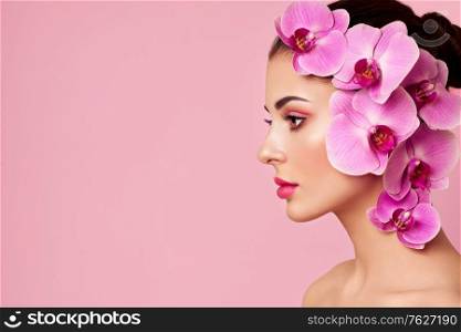Portrait of beautiful young woman with orchid. Brunette woman with luxury makeup. Perfect skin. Eyelashes. Cosmetic eyeshadow. Purple flowers