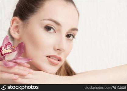 Portrait of Beautiful Young Woman with Pink Orchid looking at Camera.