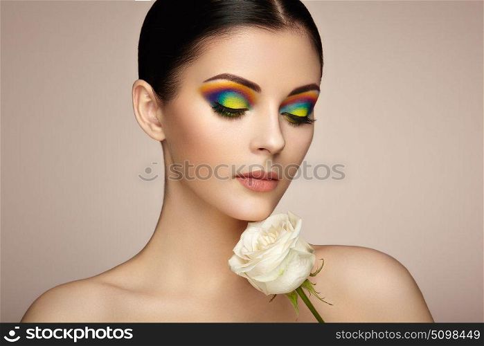 Portrait of beautiful young woman with rainbow make-up. Girl summer. Long eyelashes, vivid colorful eyeshadows. White rose. Multicolored