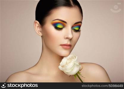 Portrait of beautiful young woman with rainbow make-up. Girl summer. Long eyelashes, vivid colorful eyeshadows. White rose. Multicolored