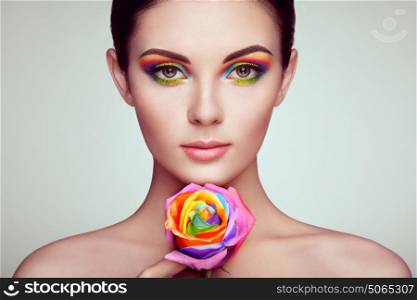 Portrait of beautiful young woman with rainbow rose. Bright colors. Long eyelashes, vivid colorful eyeshadows. Rainbow make up. Multicolored flowers