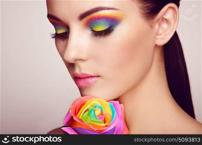 Portrait of beautiful young woman with rainbow rose. Bright colors. Long eyelashes, vivid colorful eyeshadows. Rainbow make up. Multicolored flowers
