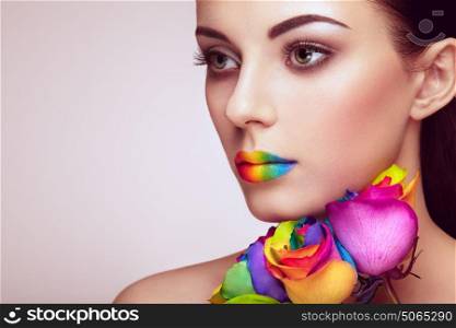 Portrait of beautiful young woman with rainbow rose. Bright colors. Vivid colorful lips. Rainbow make up. Multicolored flowers