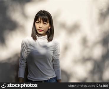 portrait of beautiful younger asian woman standing against white wall