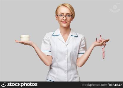 Portrait of beauty specialist standing against grey background and holding in her hand a face cream jar and measure tape.. Portrait of beauty specialist standing against grey background and holding in her hand a face cream jar and measure tape