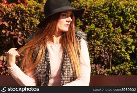 Portrait of beauty woman in hat. Gorgeous stylish young woman wearing fashionable clothes. Portrait of girl in black hat sitting on bench in park.