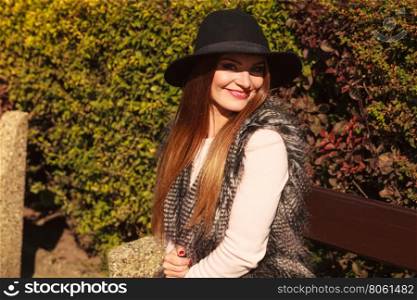 Portrait of beauty woman in hat. Gorgeous stylish young woman wearing fashionable clothes. Portrait of girl in black hat sitting on bench in park.