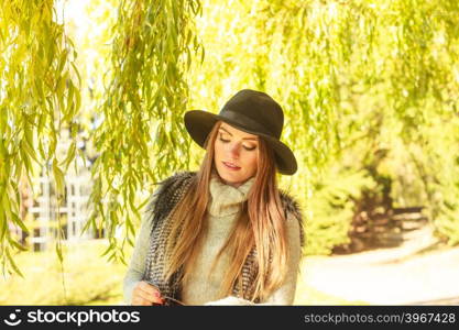 Portrait of beauty woman outdoors. Lovely cute gorgeous woman wearing black hat fur waistcoat sweater posing around leaves of willow tree in park.