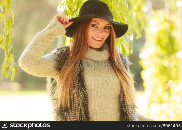 Portrait of beauty woman outdoors. Lovely cute gorgeous woman wearing black hat fur waistcoat sweater posing around leaves of willow tree in park.