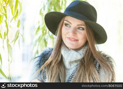 Portrait of beauty woman outdoors. Lovely cute gorgeous woman wearing black hat fur waistcoat sweater posing around leaves of willow tree in park.
