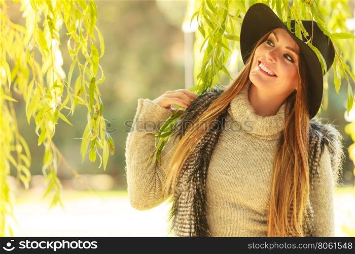 Portrait of beauty woman outdoors. Lovely cute gorgeous woman wearing black hat fur waistcoat sweater posing around leaves of willow tree in park.